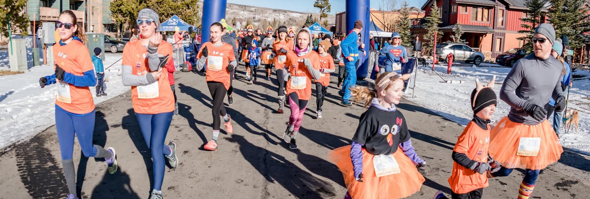 Men, women, and children dressed in orange as they run down a street in Frisco, CO for the Turkey Day 5K
